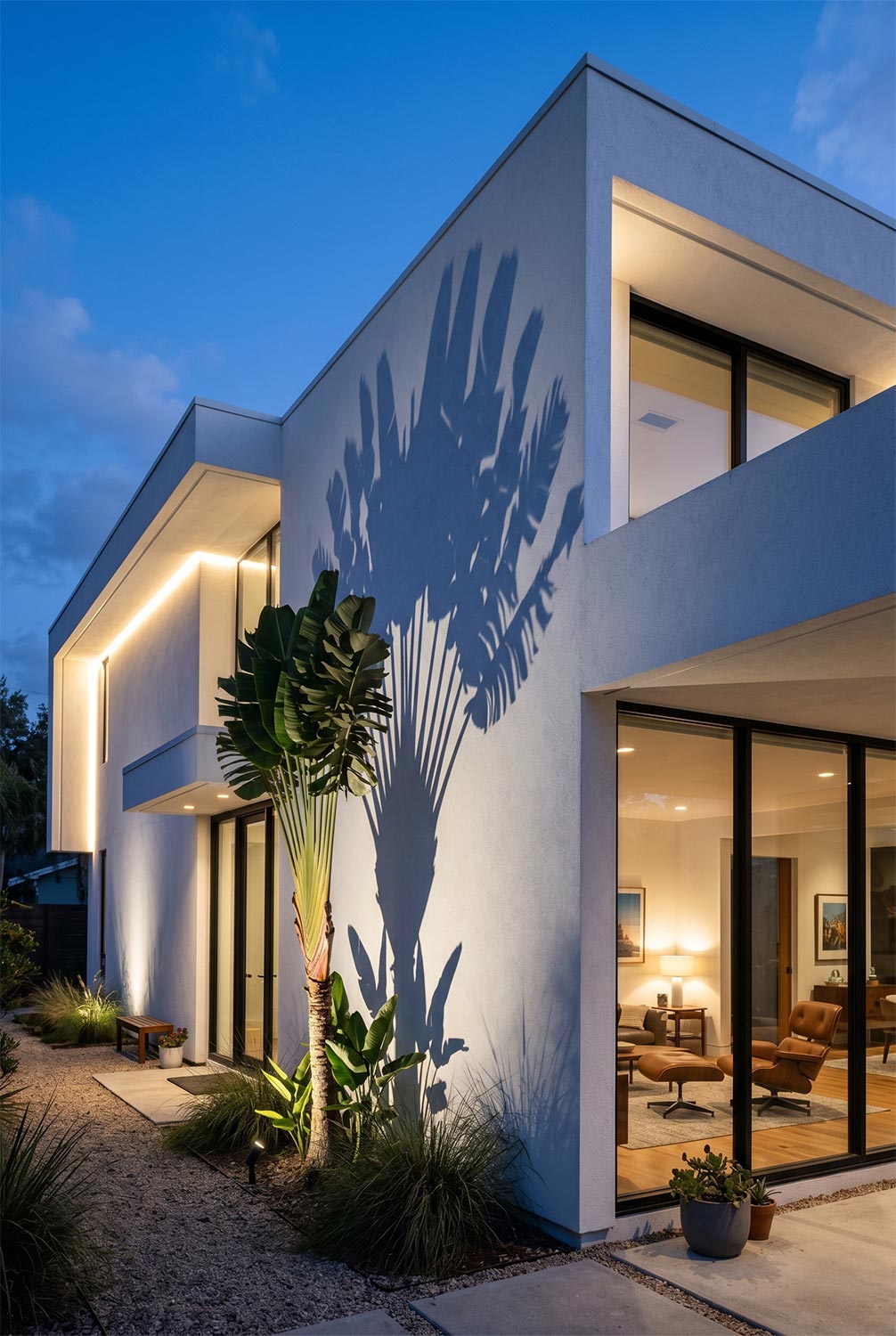 Modern white home with palm tree shadow and warm exterior lighting
